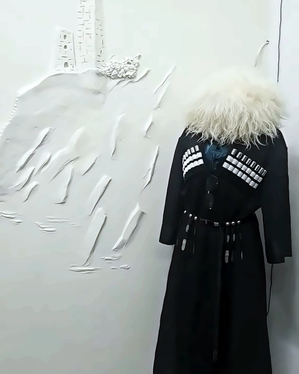 Tscherkeska mit weißer Papacha vor der Relief-Wand mit Wehrturm